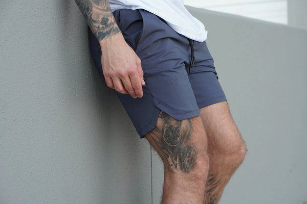 Person wearing gray-blue shorts with visible tattoos on a plain background