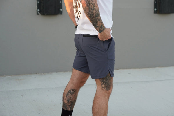 Person wearing light blue shorts with a tattooed arm against a plain background