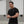 Man wearing a black t-shirt with a white No Straight Path® logo, standing indoors with gray walls and windows.
