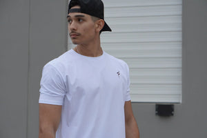 Man wearing a white t-shirt with a small No Straight Path® logo and a black cap, standing against a plain background.