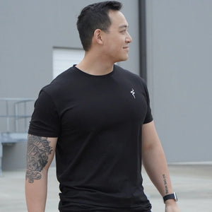 Man wearing a black t-shirt with a No Straight Path® logo, standing outdoors.