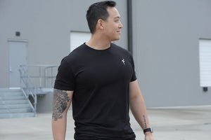 Man wearing a black t-shirt with a No Straight Path® logo, standing outdoors.