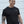 Man smiling wearing a black t-shirt with a No Straight Path® logo, standing against a white wall.