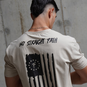 Person wearing a white t-shirt with a black flag design and a No Straight Path® text against concrete wall.