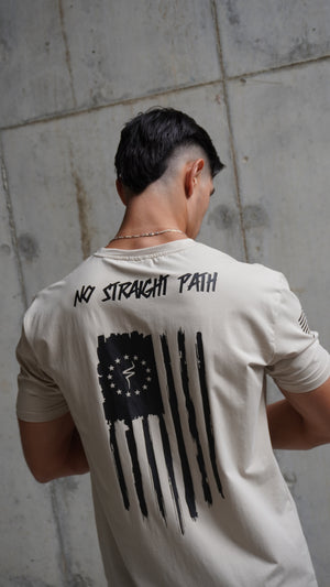 Person wearing a white t-shirt with a black flag design and a No Straight Path® text against concrete wall.