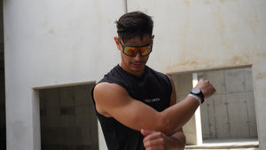 Man wearing black sleeveless shirt and sunglasses flexing his arm in a neutral setting