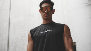 Man wearing a black sleeveless shirt with text and reflective sunglasses against a light background