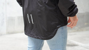 Person wearing a black jacket with white reflective stripes on a neutral background