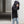 Person wearing a black jacket and jeans standing in an urban setting.