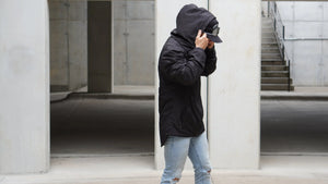 Person wearing a black jacket and jeans standing in an urban setting.