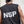 Person wearing a sleeveless shirt with 'NSP' on the back against a concrete wall.