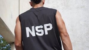 Person wearing a sleeveless shirt with 'NSP' on the back against a concrete wall.