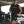 Man running in a parking lot wearing a black sleeveless shirt and shorts with visible text.