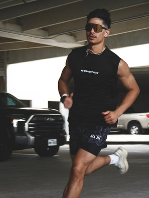 Man running in a parking lot wearing a black sleeveless shirt and shorts with visible text.