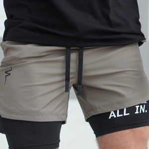 Person wearing gray shorts with a black waistband and 'All In' text on a light background