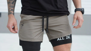 Person wearing gray shorts with a black waistband and 'All In' text on a light background