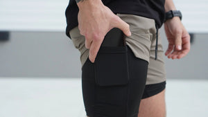 Person wearing black shorts with a phone pocket, standing on a light background