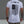Person wearing a white t-shirt with a black graphic design on the back, standing against a gray background.