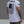 Person wearing a white t-shirt with a black flag design and text on the back, standing against a gray background.