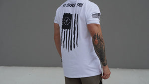 Person wearing a white t-shirt with a black flag design and text on the back, standing against a gray background.