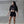 Woman wearing a black crop top and shorts with visible branding against a concrete wall.