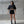 Woman wearing a black crop top and shorts standing against a concrete wall.