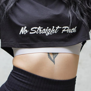 Person wearing a black crop top with 'No Straight Path' text, white underwear, and black pants.