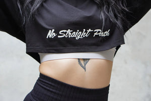 Person wearing a black crop top with 'No Straight Path' text, white underwear, and black pants.