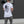 Person wearing a white t-shirt with a design on the back, standing against a dark wall.