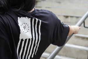 Person wearing a black t-shirt with a white flag design on the back, standing on steps.