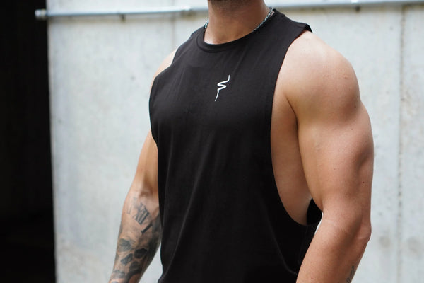 Person wearing a black tank top with a No Straight Path® logo, standing against a light-colored wall.