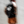 A person wearing a black shirt with a large white 'NSP' logo on the back, paired with orange shorts and a dark cap, captured in a motion-blurry double-exposure style against a light gray concrete wall.