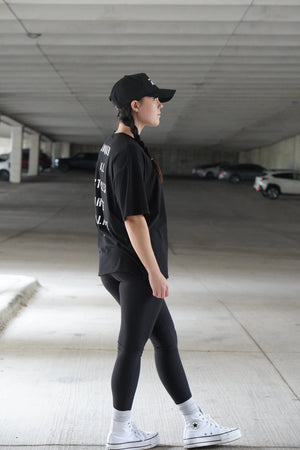 Person wearing a black outfit with white sneakers in an underground parking lot.