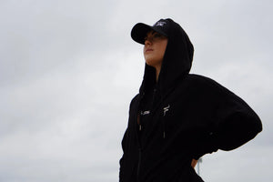 Person wearing a black hoodie and cap against a gray sky