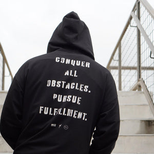 Person wearing a black hoodie with motivational text on the back, standing on stairs.
