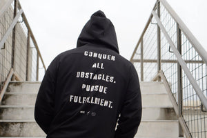 Person wearing a black hoodie with motivational text on the back, standing on stairs.