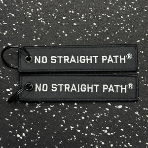 Black keychain with No Straight Path® text on a speckled black and white background