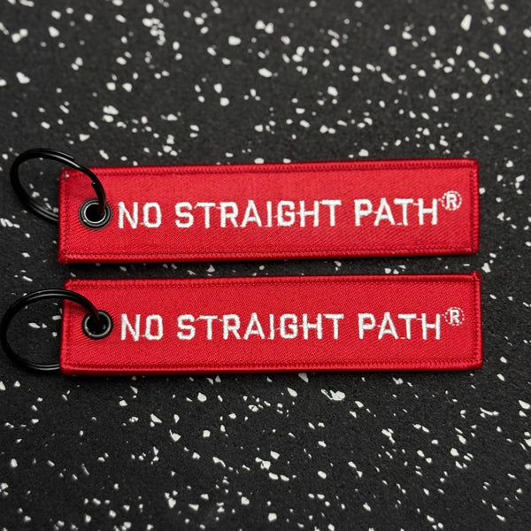 Two red No Straight Path® keychains on a black speckled background