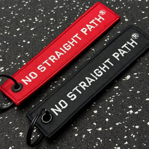 Two No Straight Path® keychains, one red and one black, on a textured black background.