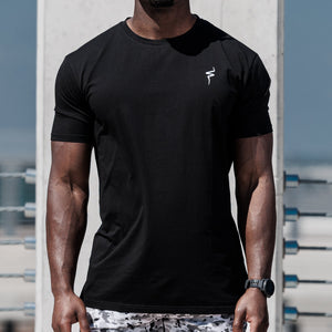 Man wearing a black t-shirt and patterned shorts standing outdoors.