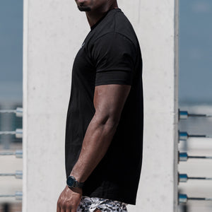 Man wearing a black t-shirt, patterned shorts, and white sneakers on a rooftop.