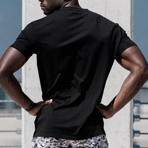 Man in black t-shirt and patterned shorts standing on a rooftop with a cityscape background