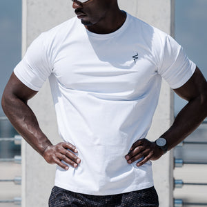 Man wearing a white t-shirt and black shorts standing on a rooftop with a cityscape background