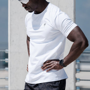 Man wearing a white t-shirt, black shorts, and white sneakers standing outdoors.