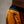 Close-up of a person wearing orange athletic shorts with a black waistband and a small black zipper pocket detail, photographed against a neutral beige background.